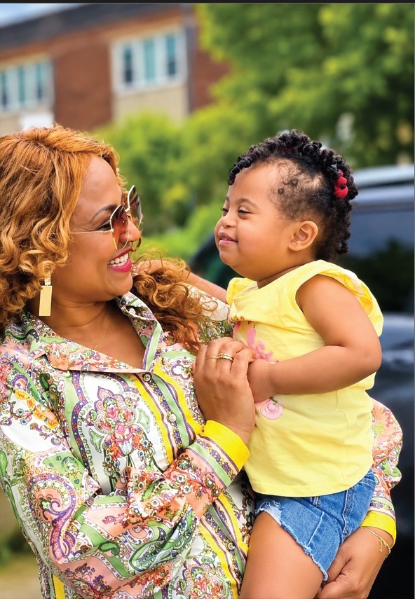 A smiling woman holding a young child outdoors