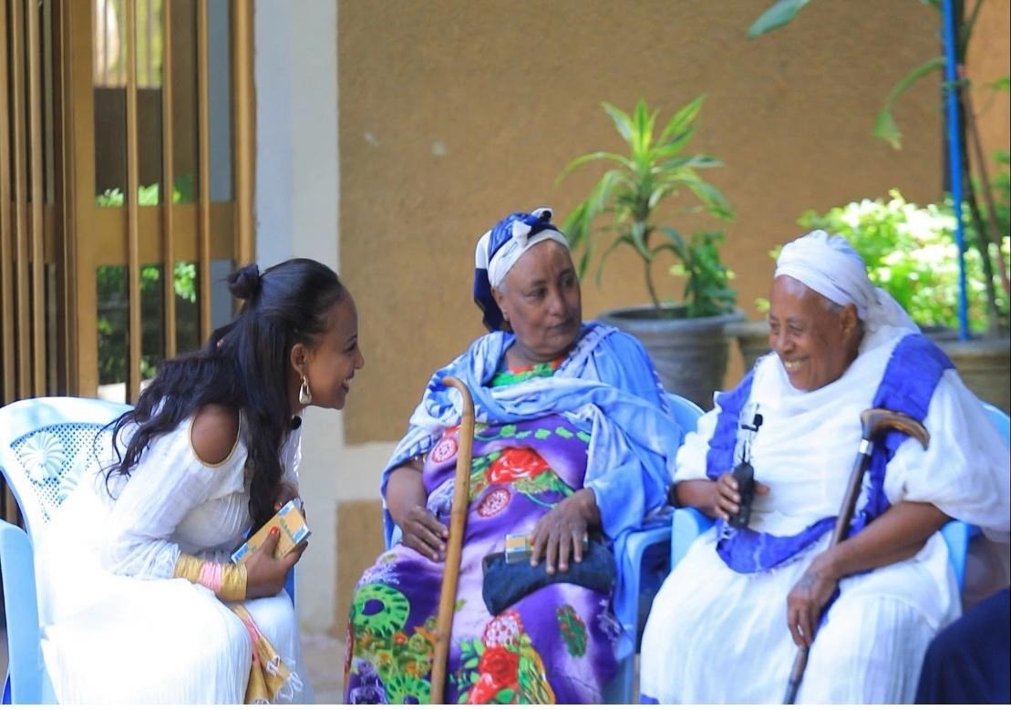 A woman talking with two elderly women seated outdoors