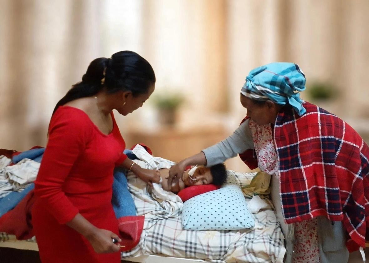 Two women caring for a person lying in bed