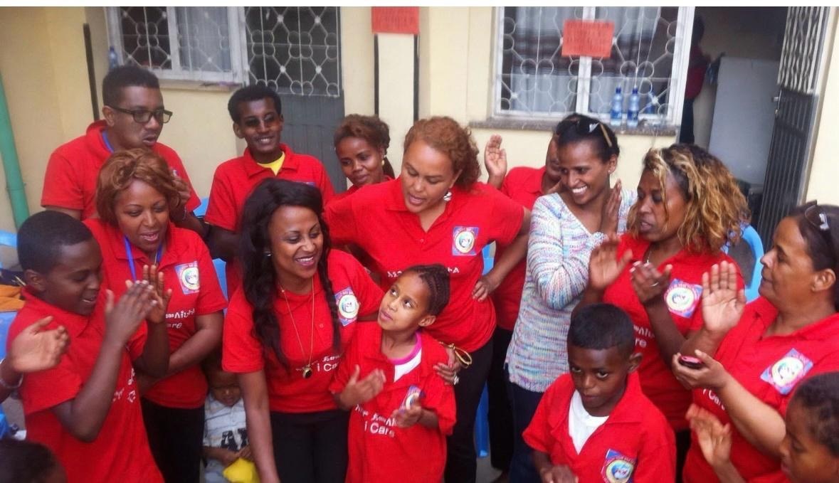 A group in matching red shirts gathered with children, clapping together